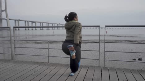 Back-view-of-young-woman-warming-up-before-training-on-wooden-pier